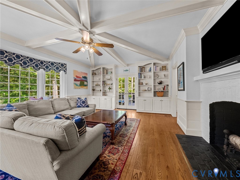 Vaulted ceiling featuring exposed beams, wood-finish flooring, built-in cabinetry, and a fireplace with a black masonry hearth