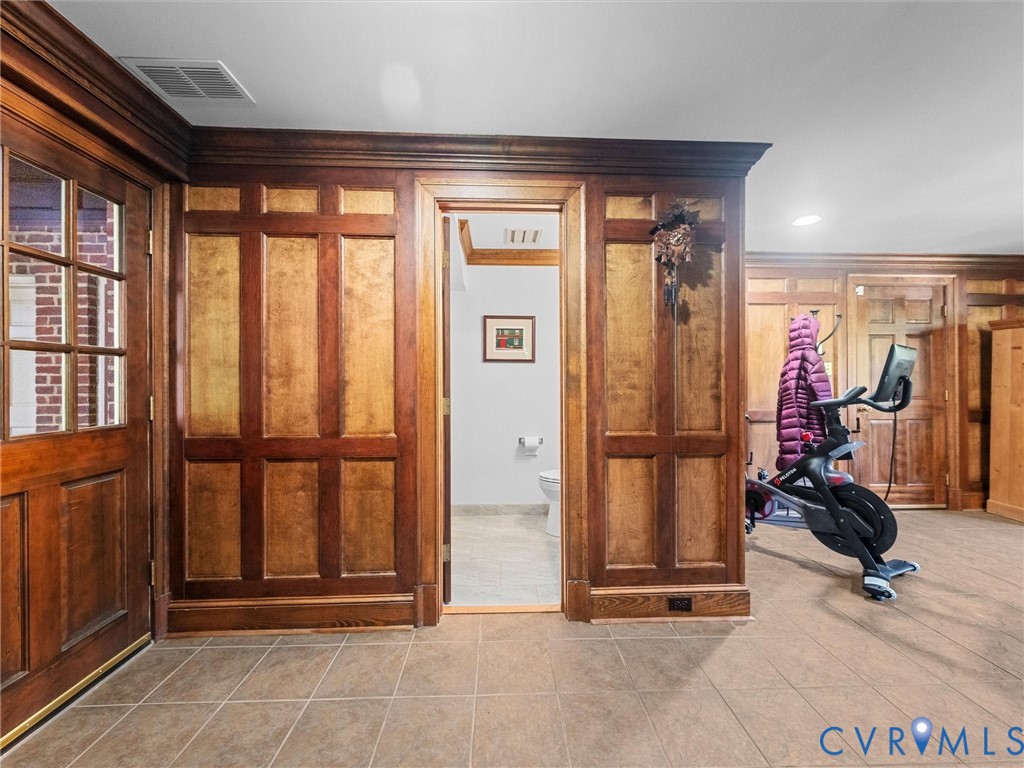 Custom wood wainscoting with integrated crown molding, solid wood paneled doors, and ceramic tile flooring