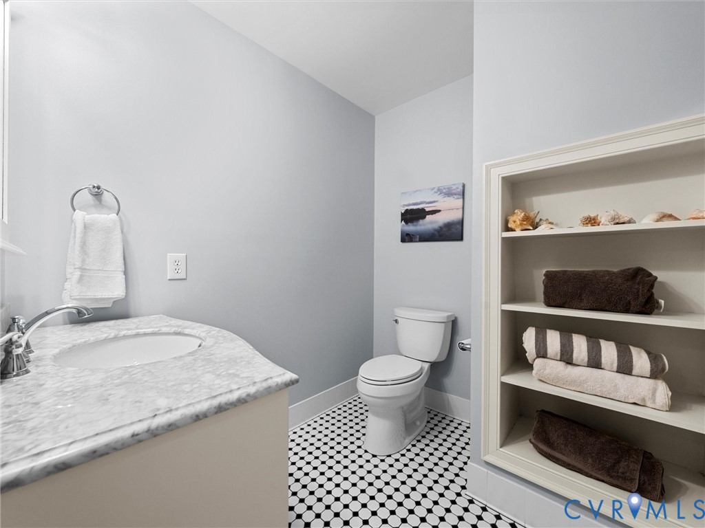 Vanity featuring a stone countertop and integrated oval sink, complemented by black and white mosaic tile flooring, a wall-mounted ring towel holder, and built-in recessed shelving