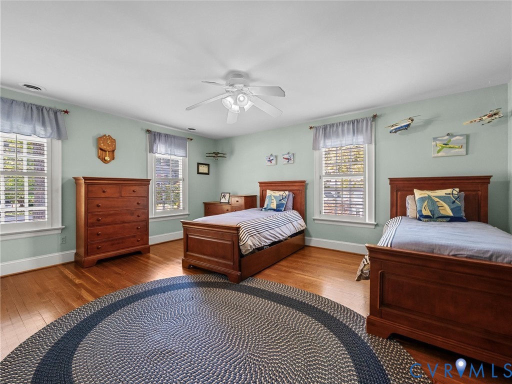 Spacious room featuring wood-finish flooring, three double-hung windows, and a ceiling-mounted light fixture with a central fan
