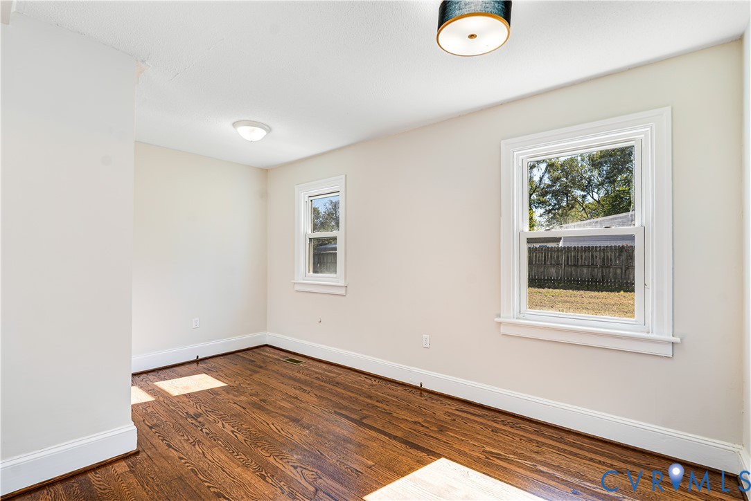 Room featuring wood-finish flooring, dual windows with decorative trim, and a drum-style ceiling light fixture