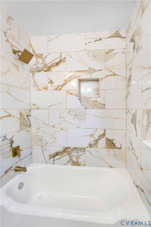 Shower and bathtub combination featuring large-format wall tile with veined patterning, gold-tone plumbing fixtures, and an integrated recessed soap niche