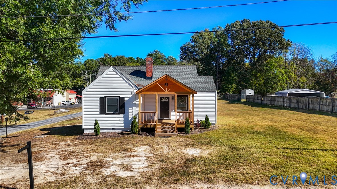 White siding exterior with a red brick chimney, covered front porch featuring wood-post supports, and an expansive side yard enclosed by wood fencing