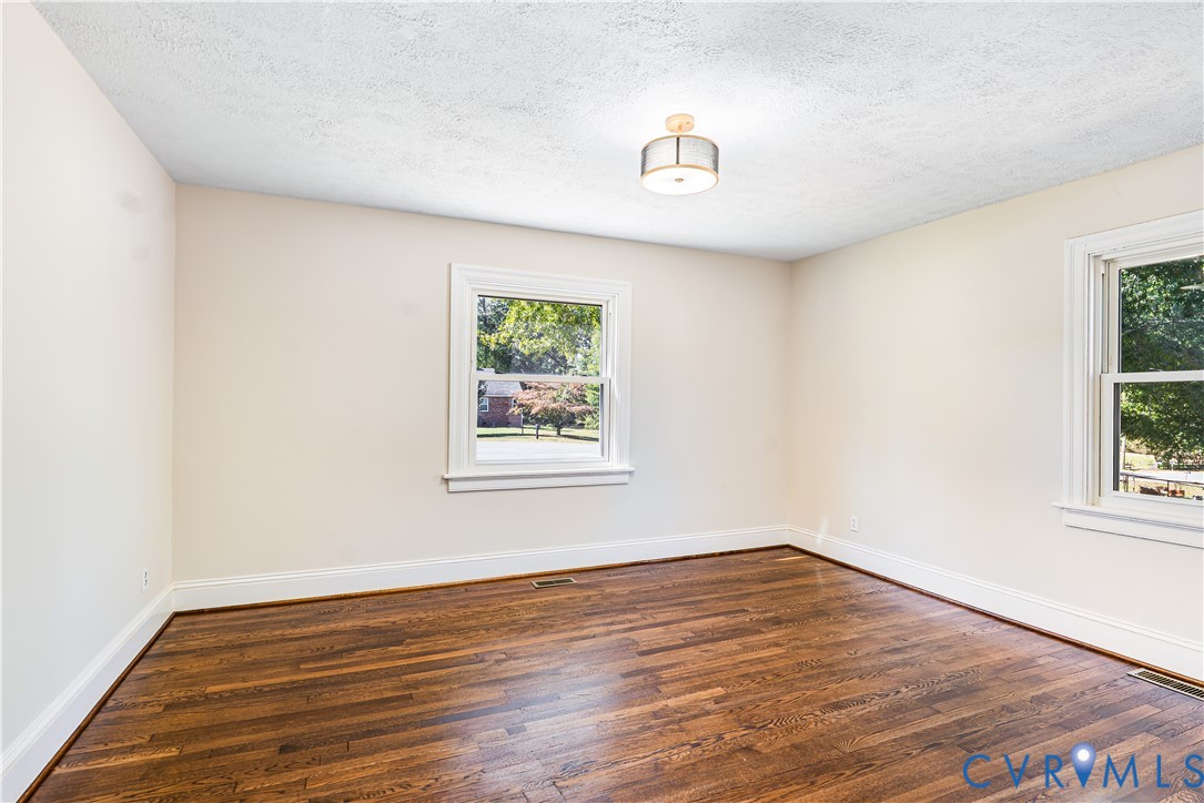 Room with wood-finish flooring, two double-hung windows, and a flush-mount drum ceiling light fixture