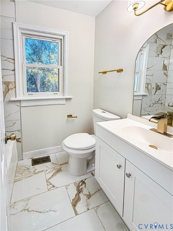 Bathroom featuring large-format tile flooring with gold veining, white vanity with integrated sink, brass-tone hardware and lighting, and arched mirror