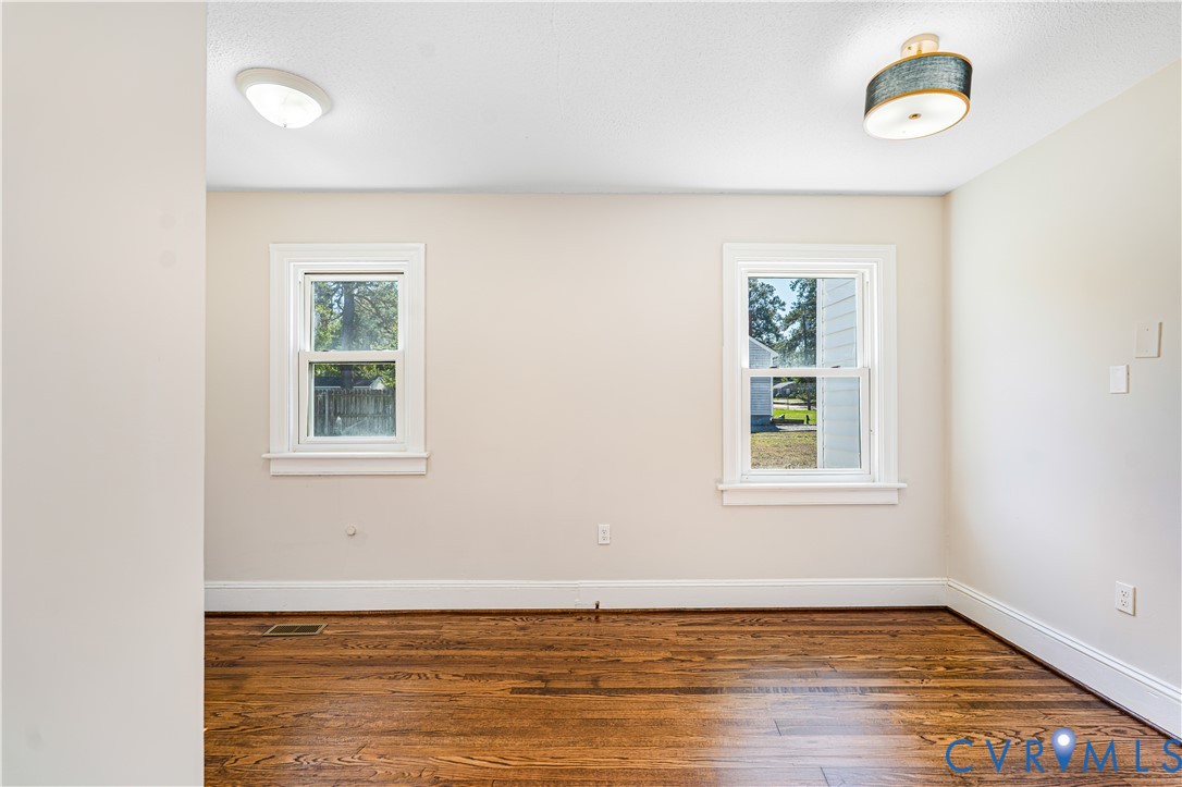 Room featuring wood-finish flooring, two double-hung windows with white trim, and overhead lighting fixtures