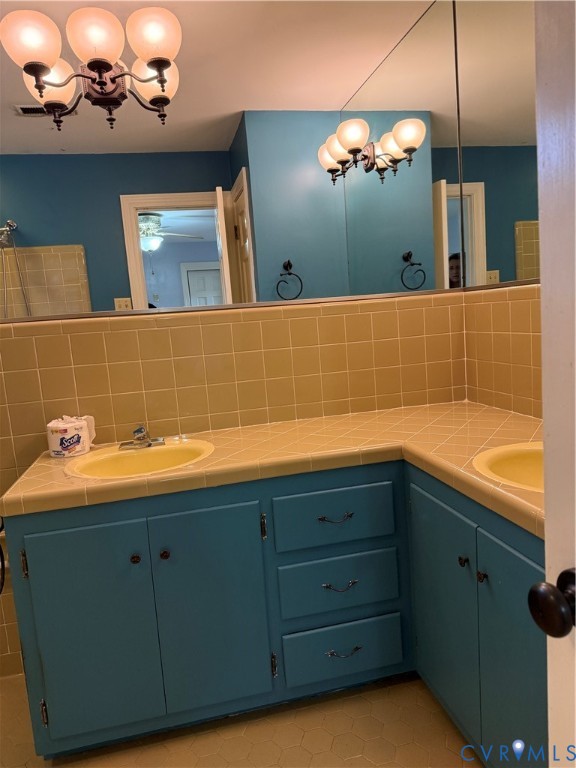 L-shaped vanity featuring dual integrated sinks, tile countertop, expansive wall-mounted mirror, and multi-light globe fixture