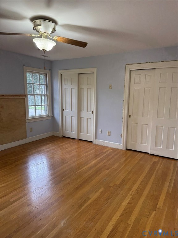 Room featuring wood-finish flooring, two sets of multi-panel sliding closet doors, a multi-pane window, and a central ceiling fan with integrated lighting