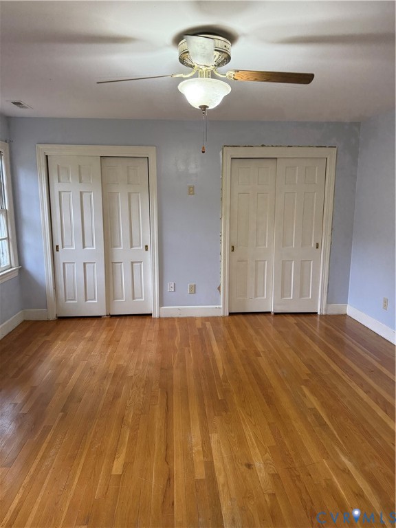 Wood-finish flooring, two sets of paneled closet doors, and a ceiling-mounted light fixture with a fan