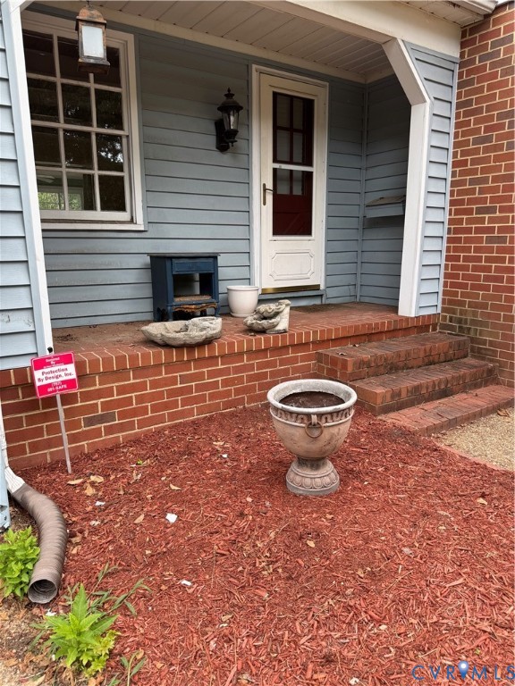 Covered front porch featuring brick masonry steps, horizontal siding, and classic exterior wall-mounted lighting