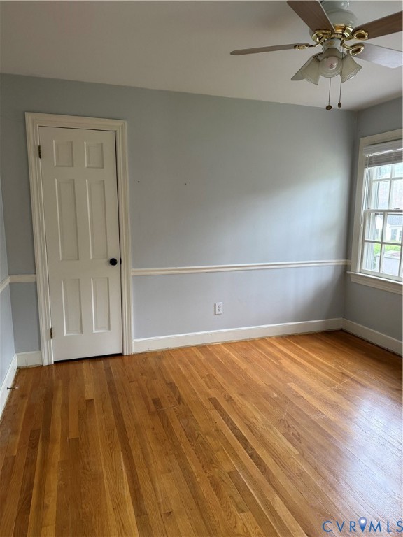 Room featuring wood-finish flooring, chair rail molding, a six-panel door, and a ceiling fan with integrated lighting
