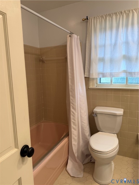 Bathroom featuring a porcelain tub, neutral-tone wall tiling, hexagon-patterned floor tile, and a multi-pane window