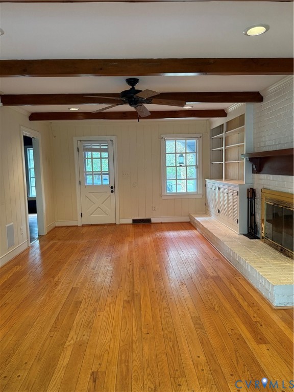 Exposed ceiling beams, wood-finish flooring, white brick fireplace with a wood mantel, built-in cabinetry, and multi-pane glass door