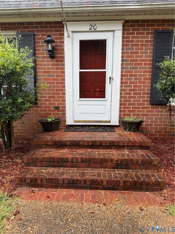 Brick exterior featuring a multi-step masonry stoop, white trim, classic louvered shutters, and a wall-mounted coach light