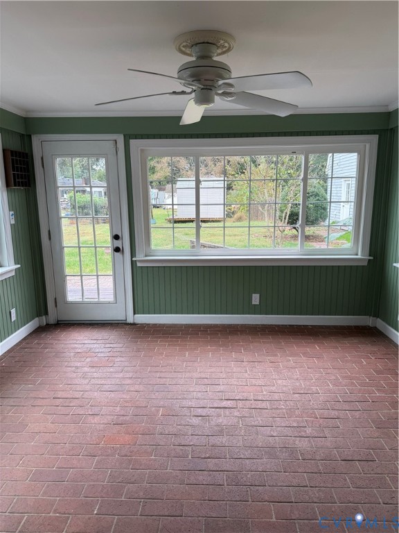 Enclosed area featuring red brick flooring, vertical paneled wall treatments, large-format picture window, white-finish ceiling fan, and glass-paneled exterior door
