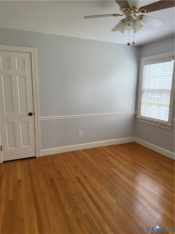 Interior room featuring wood-finish flooring, chair rail molding, a single-panel door, and a ceiling fan with integrated light fixture