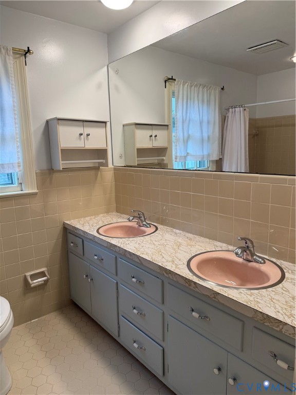 Dual-sink vanity featuring a patterned countertop, integrated oval basins, chrome-finish faucets, and extensive cabinetry with built-in wall storage, finished with hexagonal tile flooring and tile wall accents
