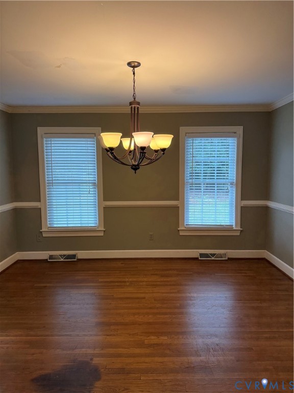 Room featuring wood-finish flooring, chair rail molding, crown molding, and a multi-arm chandelier with frosted glass shades