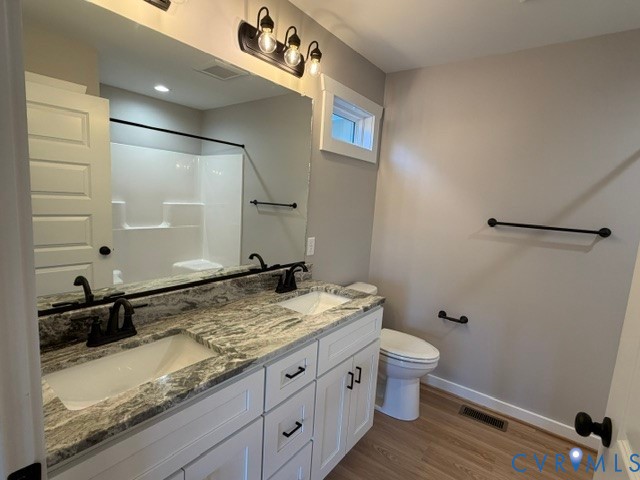 Double vanity with stone countertop, undermount sinks, matte black fixtures, white shaker-style cabinetry, and wood-finish flooring