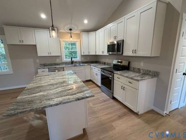 Kitchen featuring white shaker-style cabinetry, a stone countertop island, stainless steel appliances, and wood-finish flooring under a vaulted ceiling