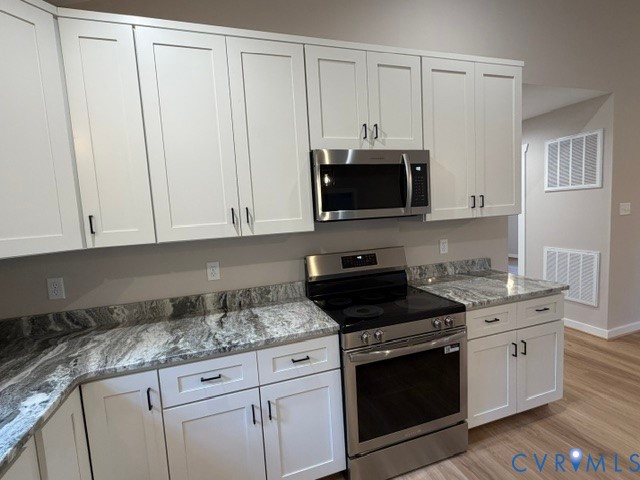 White shaker-style cabinetry with matte black hardware, stone-patterned countertops, stainless steel electric range, and stainless steel microwave