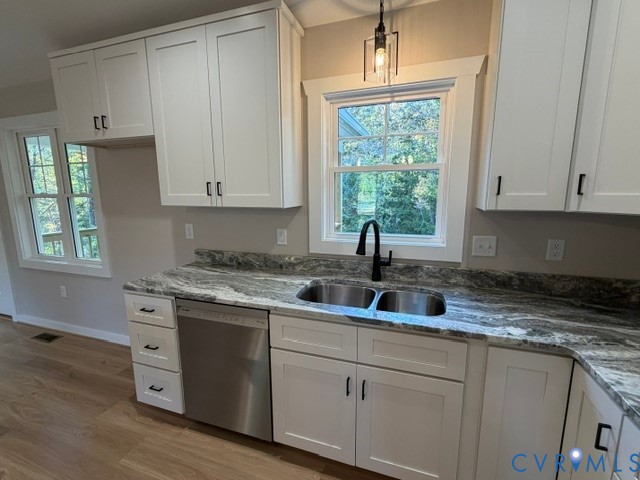 Kitchen featuring white shaker-style cabinetry, patterned stone-surface countertops, stainless steel undermount double-basin sink with matte black faucet, and wood-finish flooring