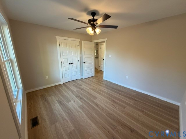 Room featuring wood-finish flooring, multi-pane window, ceiling fan with light fixture, and paneled doors