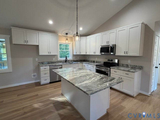Kitchen featuring white shaker-style cabinetry, stone-patterned countertops, a central island, stainless steel appliances, and wood-finish flooring