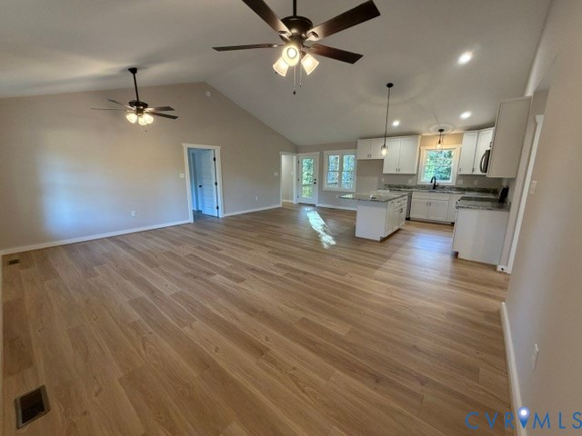 Vaulted ceilings with dual ceiling fans, wood-finish flooring, white cabinetry, a kitchen island, and recessed lighting
