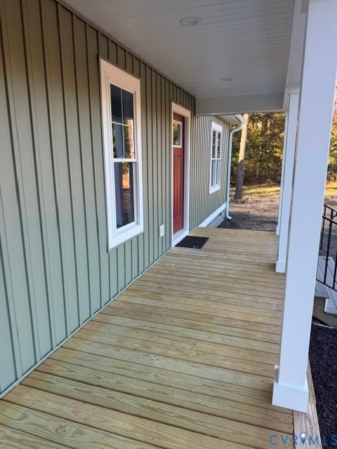 Covered front porch featuring vertical board-and-batten siding, natural wood decking, and white structural support columns