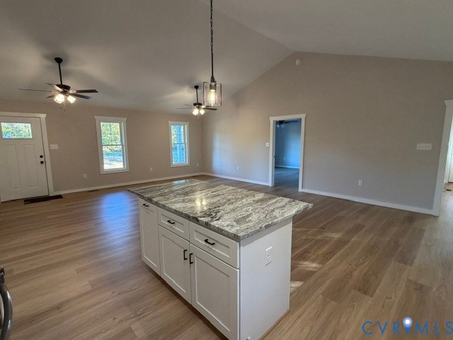Vaulted ceilings, wood-finish flooring, kitchen island with stone countertop, ceiling fans, and pendant lighting