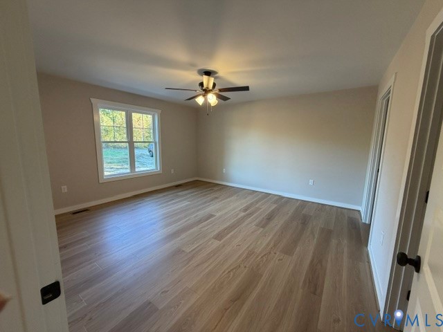 Spacious room featuring wood-finish flooring, neutral wall tones, multi-pane window, and a central ceiling fan with multi-light fixture