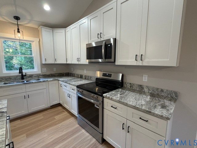 Kitchen featuring white Shaker-style cabinetry, patterned stone-surface countertops, stainless steel appliances, wood-finish flooring, and a single-handle matte black faucet
