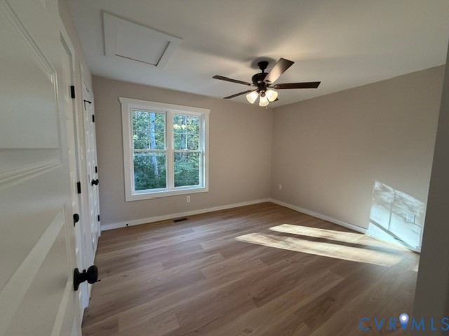 Neutral-toned interior featuring wood-finish flooring, multi-pane window, ceiling fan with light kit, and paneled doors