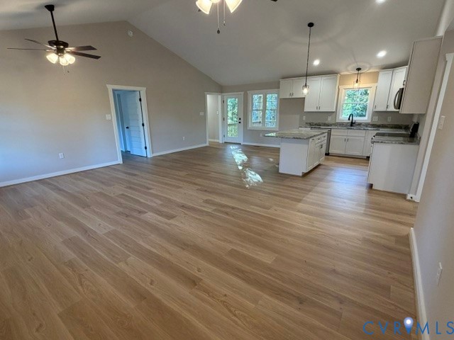 Open-concept floor plan featuring vaulted ceilings, wood-finish flooring, kitchen island, white shaker-style cabinetry, and pendant lighting