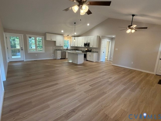 Open-concept kitchen featuring white cabinetry, a center island, stone-finish countertops, wood-finish flooring, and vaulted ceilings