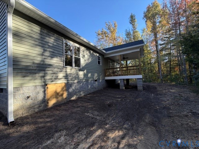 Exterior profile featuring horizontal siding, a concrete block foundation, a raised covered deck with a wooden railing, and a ceiling-mounted fan