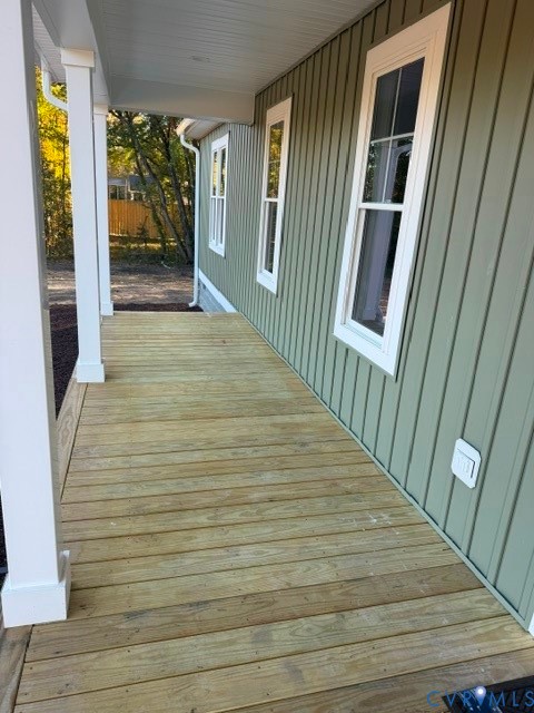 Covered porch with wood decking, vertical board siding, and square structural support columns