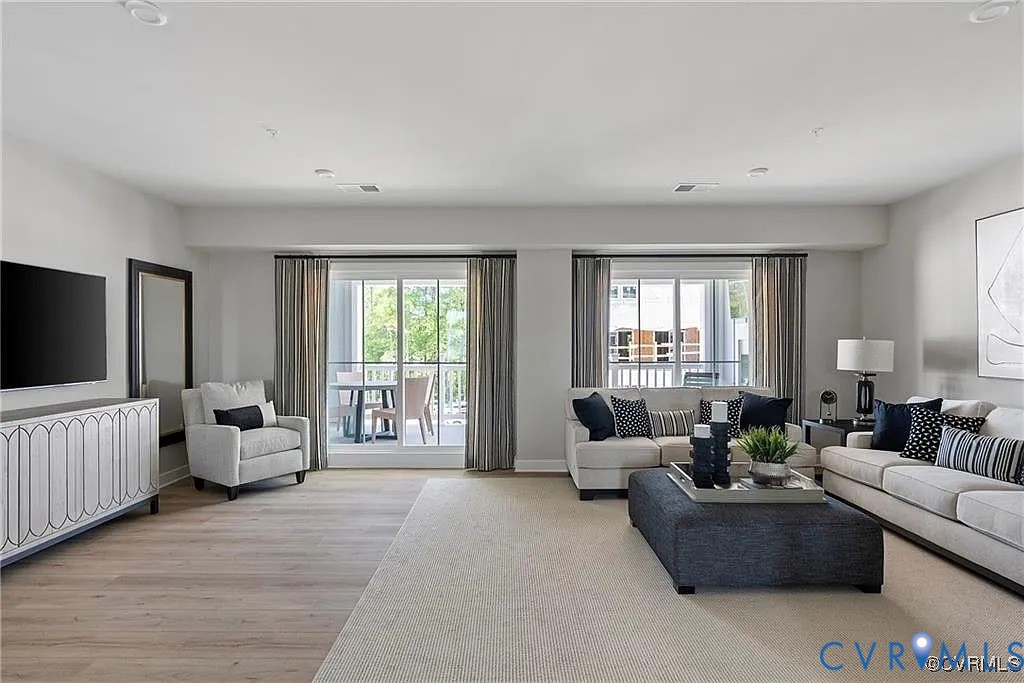 Open-concept interior featuring light wood-finish flooring, recessed lighting, and dual sets of glass sliding doors opening to an exterior balcony