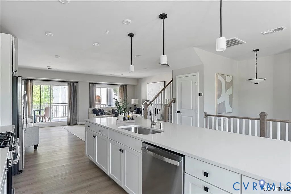 Kitchen featuring a central island with a solid surface countertop, stainless steel sink, wood-finish flooring, and pendant lighting Kitchen featuring a central island with a solid surface countertop, stainless steel sink, wood-finish flooring, and pendant lighting