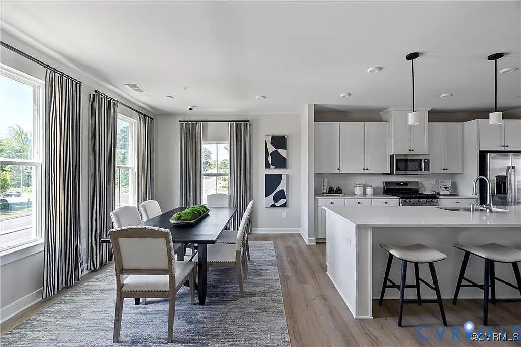 Kitchen featuring white cabinetry, an expansive center island, integrated stainless steel appliances, and wood-finish flooring Kitchen featuring white cabinetry, an expansive center island, integrated stainless steel appliances, and wood-finish flooring