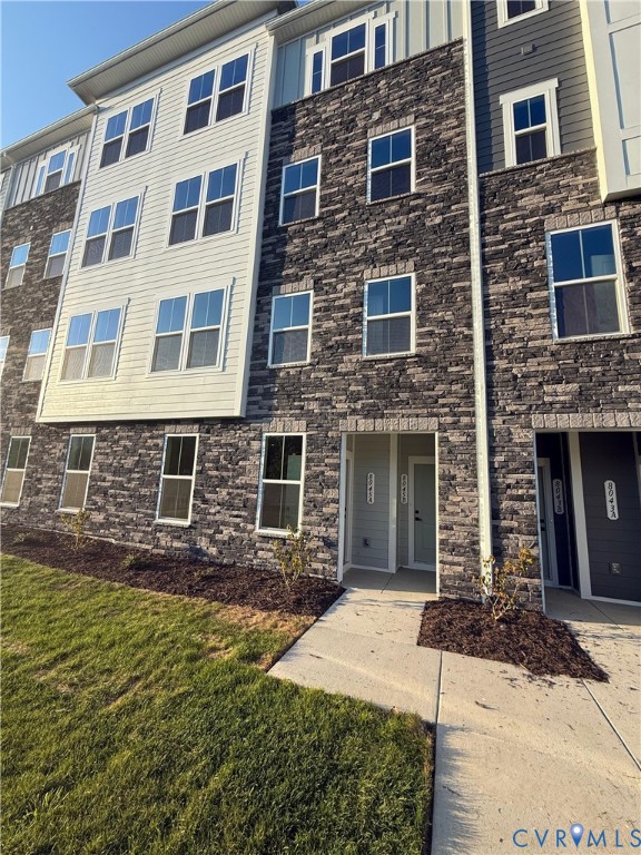 Multi-story exterior featuring stone veneer siding, horizontal lap siding, and vertical board-and-batten accents with energy-efficient windows and a concrete walkway