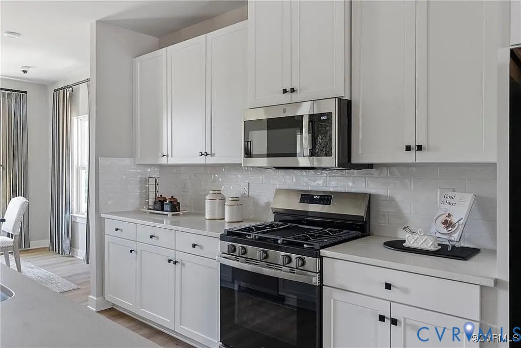 Kitchen featuring white cabinetry, subway tile backsplash, quartz countertops, stainless steel gas range, and built-in microwave Kitchen featuring white cabinetry, subway tile backsplash, quartz countertops, stainless steel gas range, and built-in microwave