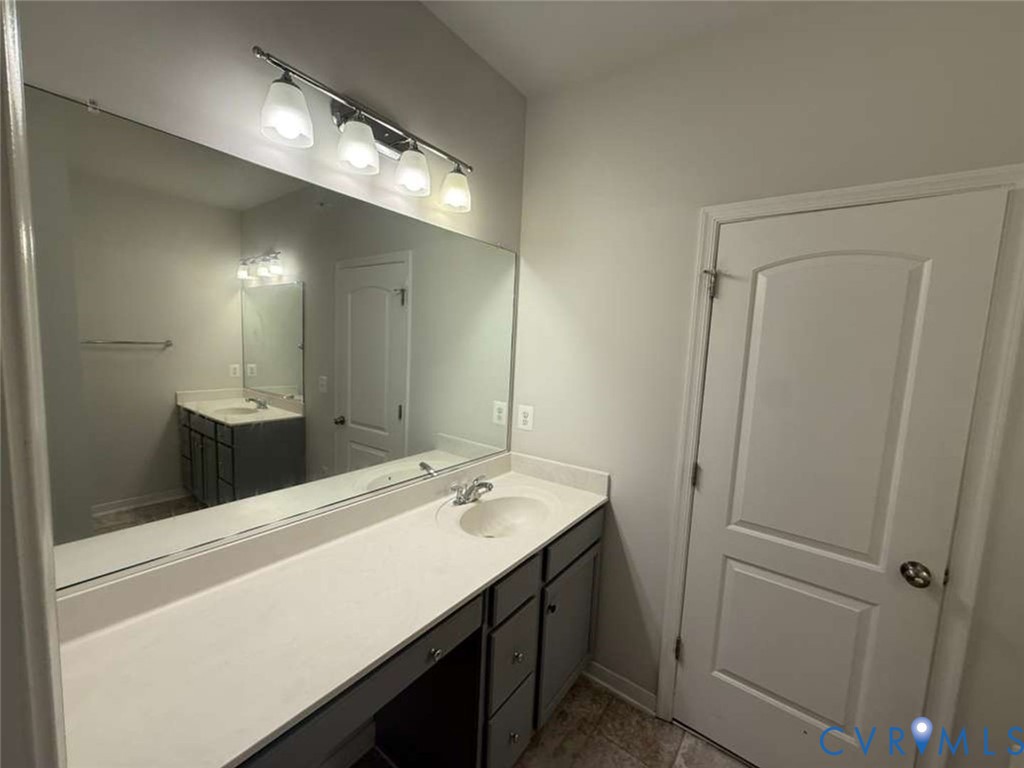 Bathroom vanity featuring a solid surface countertop with an integrated basin, charcoal-finish cabinetry, a full-width wall mirror, and a four-light fixture