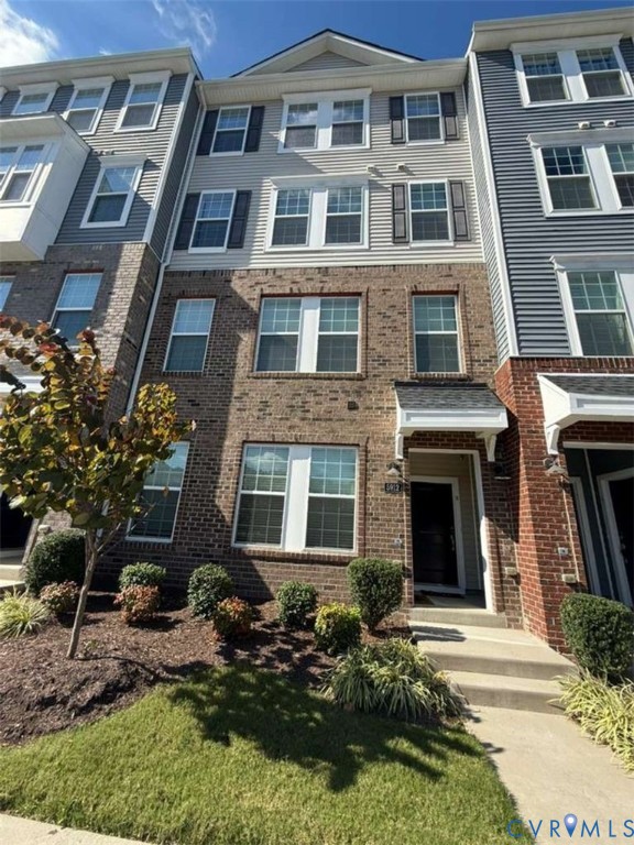 Multi-story brick and siding facade featuring multi-pane windows with shutters, a gabled roofline, and a covered entryway with a concrete walkway Multi-story brick and siding facade featuring multi-pane windows with shutters, a gabled roofline, and a covered entryway with a concrete walkway