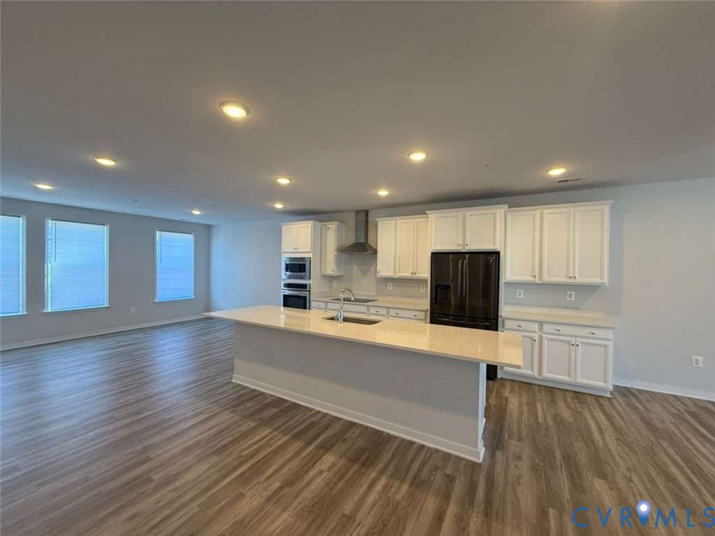 Kitchen featuring a large island with stone-finish countertops, white cabinetry, integrated stainless steel double ovens, recessed lighting, and wood-finish flooring
