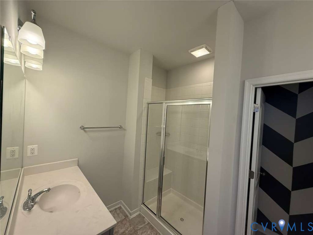 Bathroom featuring a vanity with a solid-surface countertop, an integrated sink, a glass-enclosed shower with a built-in bench, and wall-mounted light fixtures