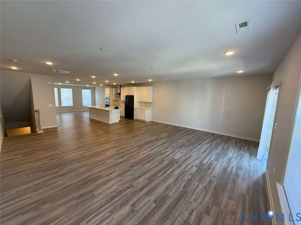 Open-concept interior featuring wood-finish flooring, recessed lighting, white cabinetry, a center kitchen island, and sliding glass doors