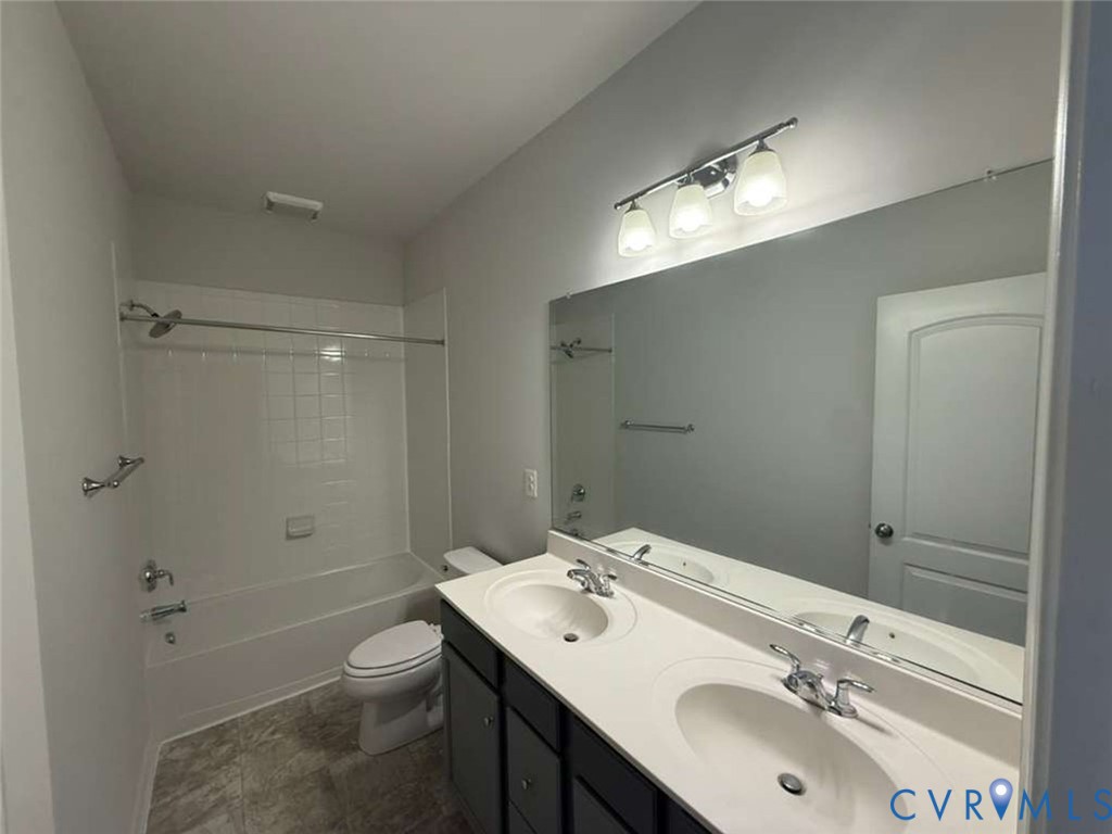 Double vanity with integrated sinks, expansive wall-to-wall mirror, three-bulb vanity lighting, and a combination tub-shower with a tiled surround