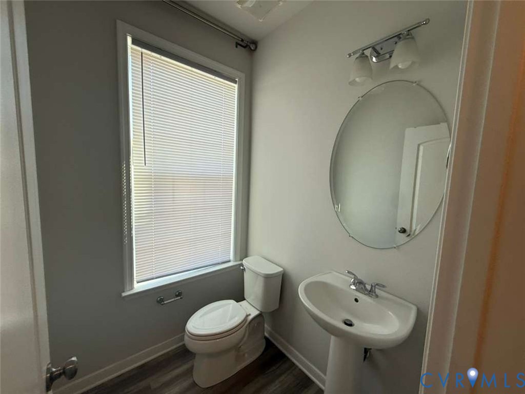 Powder room featuring a pedestal sink with a dual-handle faucet, oval frameless wall mirror, two-light vanity fixture, and wood-finish flooring